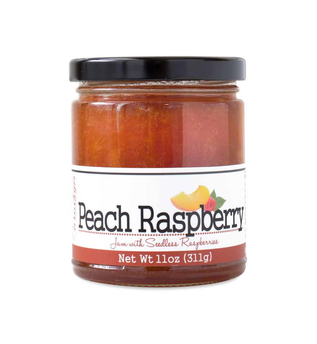 Short, lidded jar full of peach raspberry jam, on white background. The jar is labeled “Paradigm Peach Raspberry Jam with Seedless Raspberries – Net Weight 11oz (311g)”