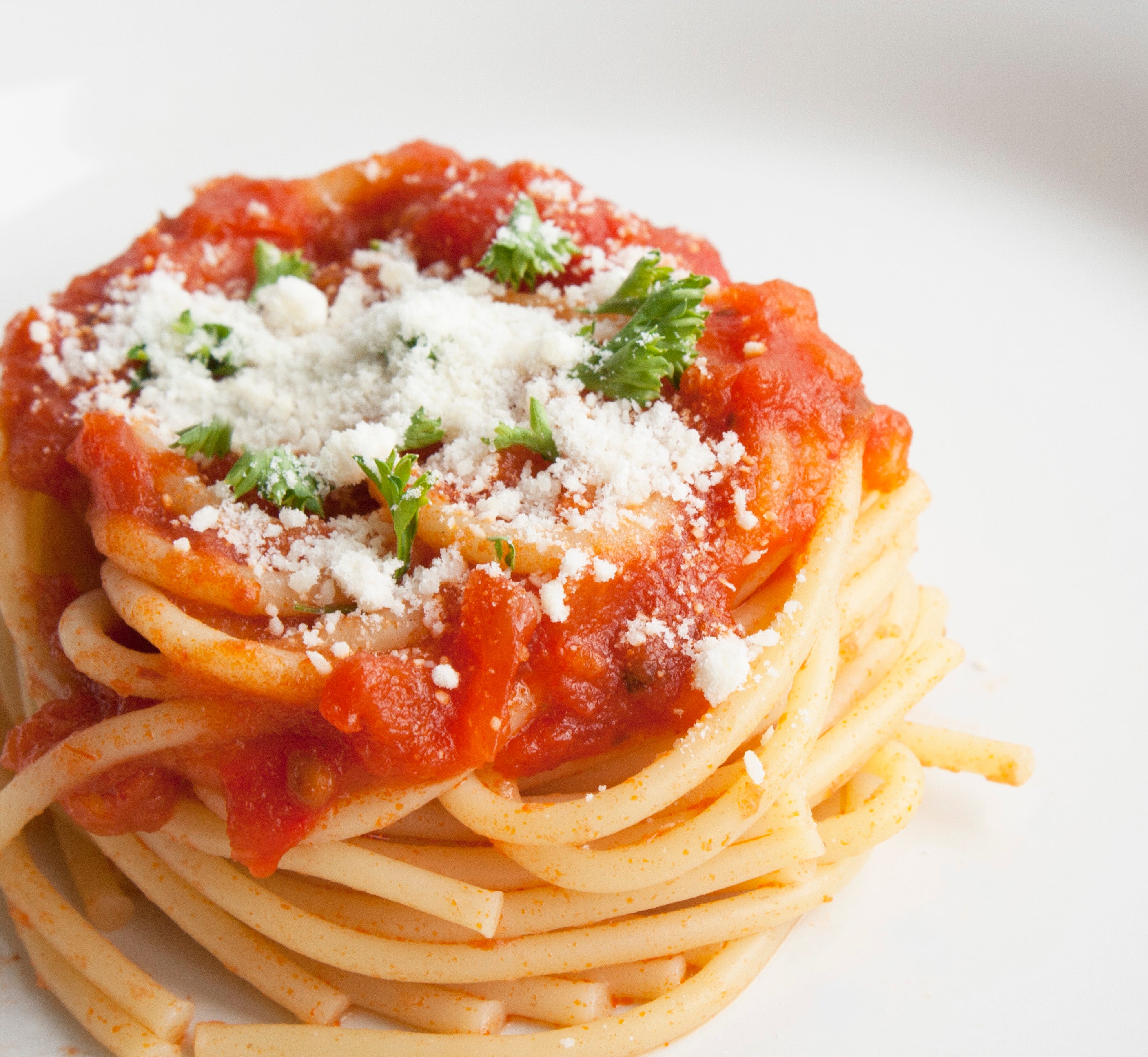 Small, neat pile of spaghetti topped with arrabbiata sauce, bits of herbs, and parmesan cheese.