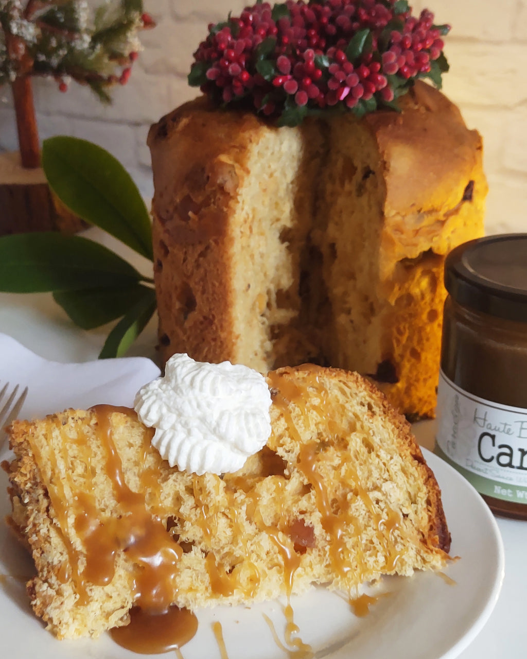 Slice of cake with paradigm foodworks haute buttered rum caramel and whipped cream on a plate, with a whole cake and a jar of caramel sauce in the background.