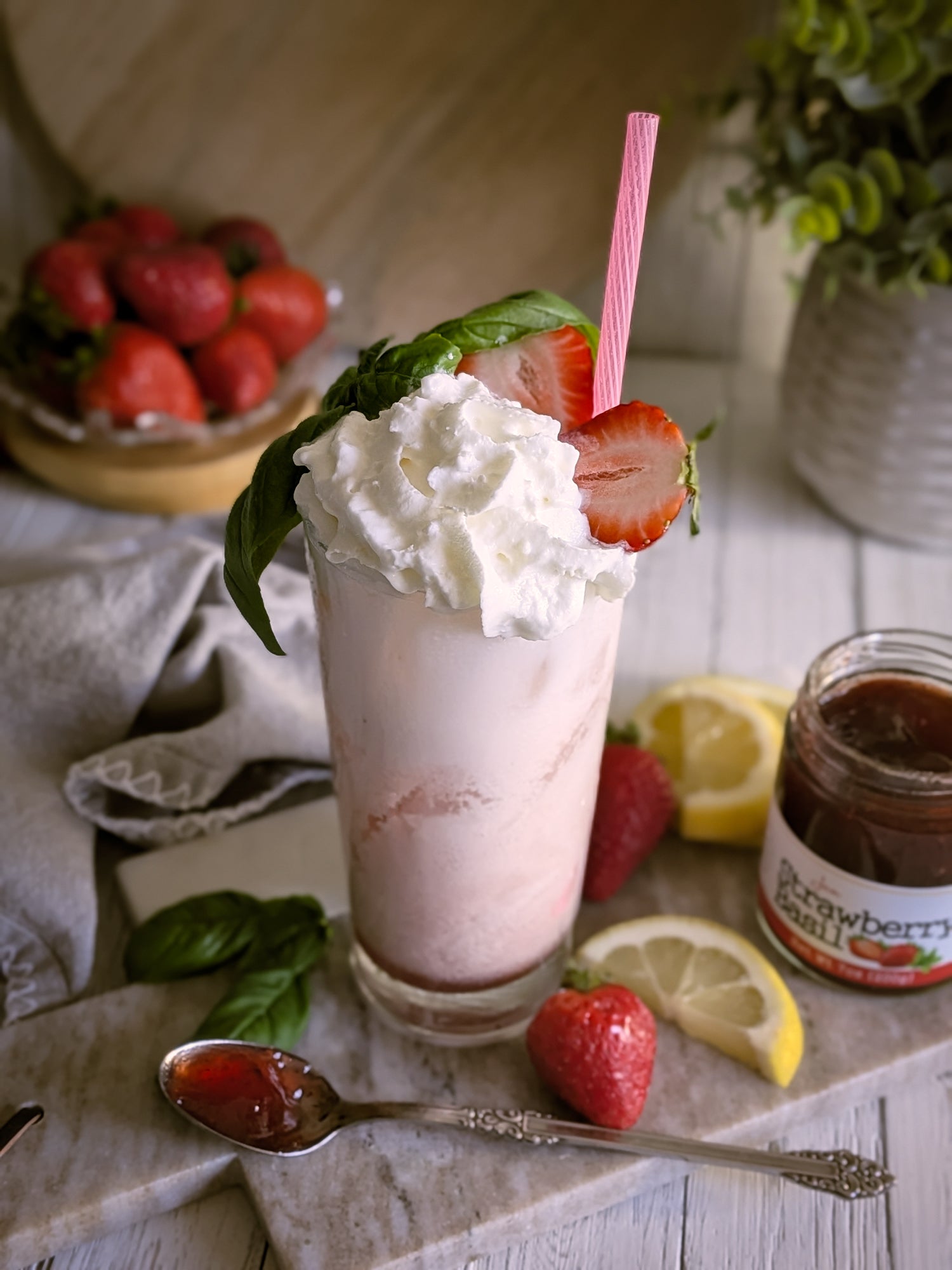 Strawberry Basil Italian Soda with whipped cream, strawberries, and a pink straw on a wooden table.