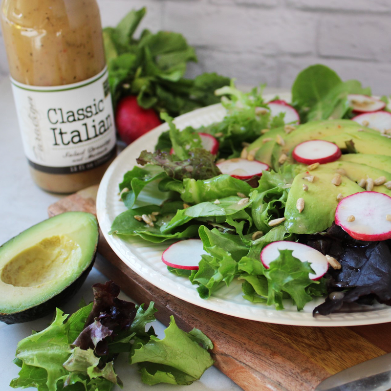 Salad containing mixed greens, avocado, sliced radishes and sunflower seeds topped with Paradigm's Classic Italian Dressing