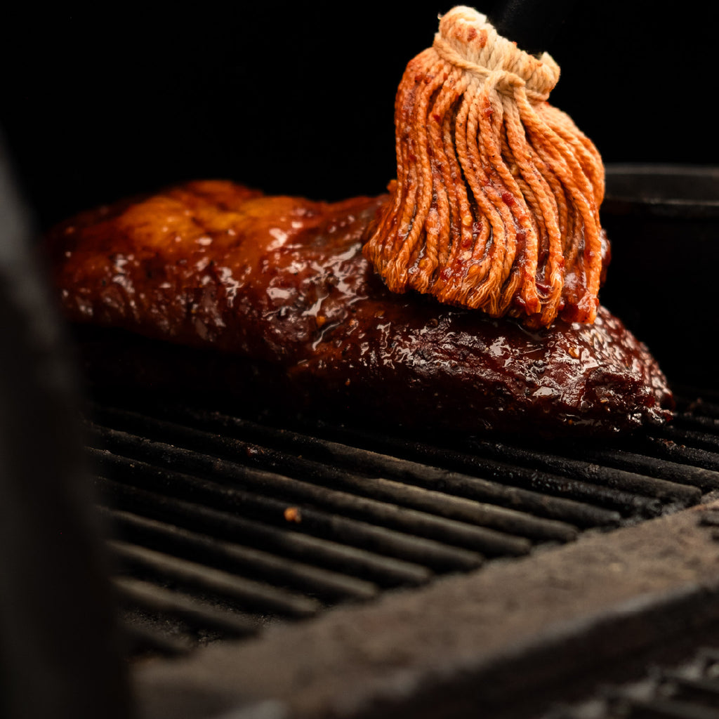 Meat on a grill being brushed by paradigm foodworks north carolina mop sauce