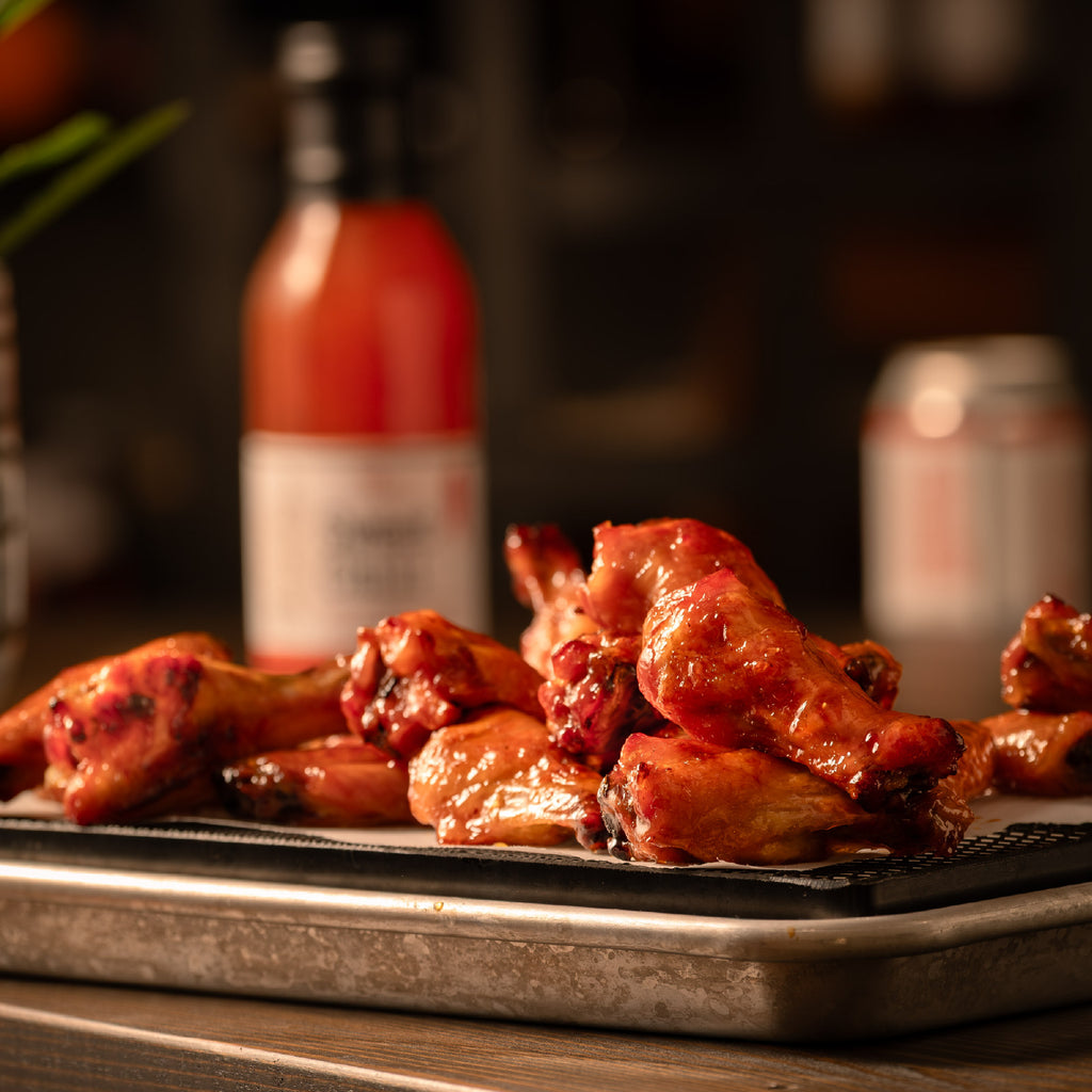 Baked chicken wings on a tray with a bottle of paradigm foodworks thai sweet chili sauce in the background