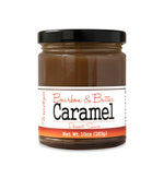 Short, lidded jar full of caramel sauce, on white background. The jar is labeled “Paradigm Bourbon & Butter Caramel Dessert Sauce – Net Weight 10oz (283g)” 