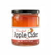 Short, lidded jar full of apple cider jam, on white background. The jar is labeled “Paradigm Brandied Apple Cider Jelly  – Net Weight 11oz (311g)”