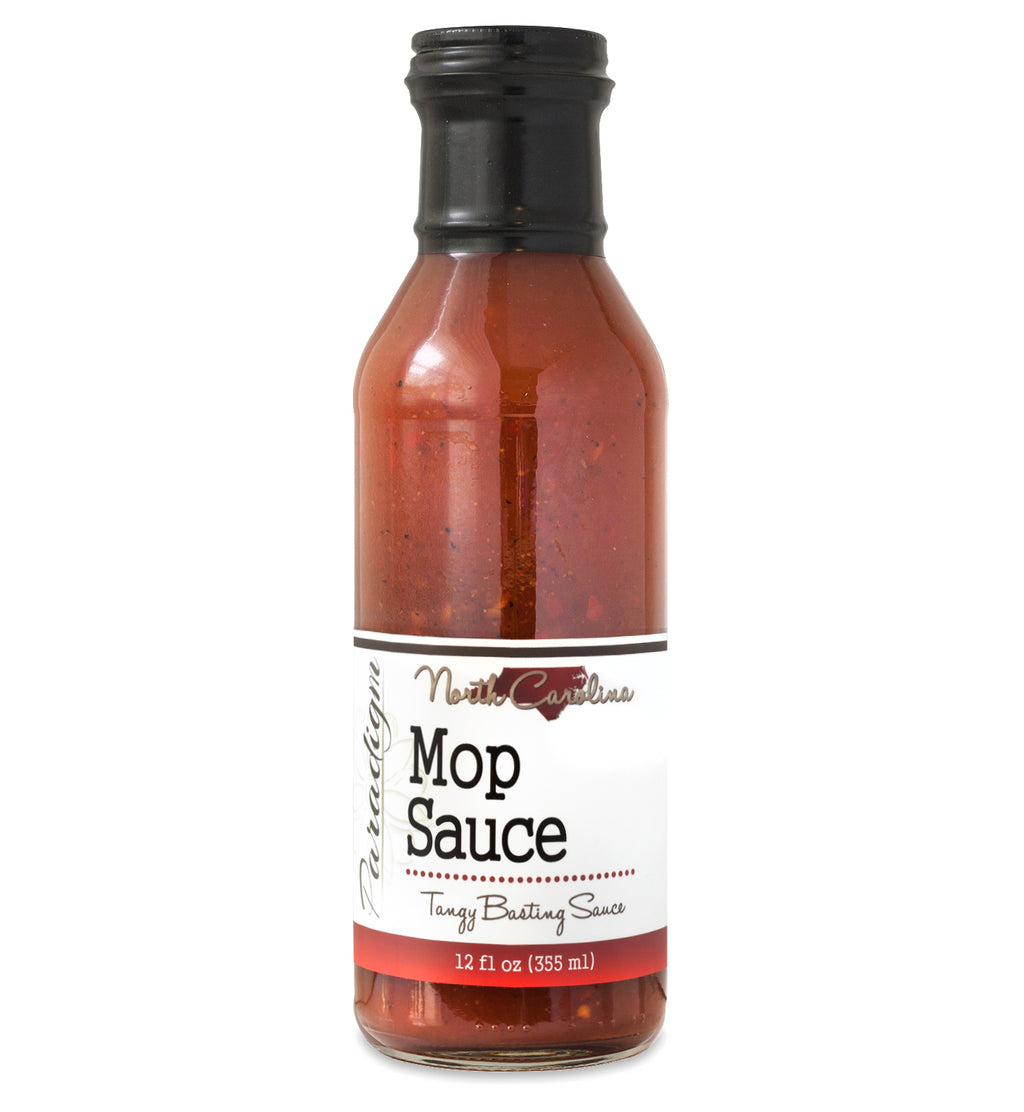 Glass ring neck bottle filled with mop sauce on white background. The bottle is labeled, “Paradigm North Carolina Mop Sauce – Tangy Basting Sauce – 12 fl oz (355ml)”