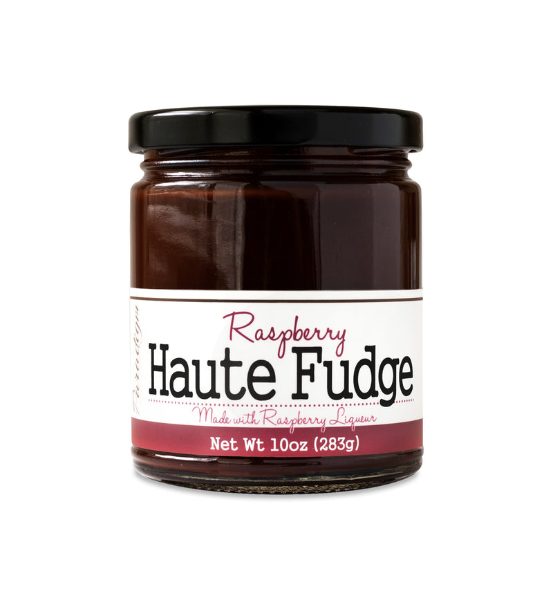 Short, lidded jar full of fudge sauce, on white background. The jar is labeled “Paradigm Raspberry Haute Fudge Made with Raspberry Liqueur– Net Weight 10oz (283g)” 