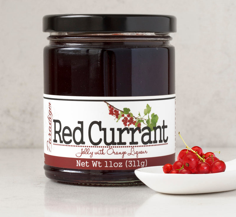 Jar of Red Currant Jelly on white countertop in front of white marble wall, with a white ceramic spoon full of currants in front of the jar on the right.