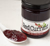 Closeup of Red Currant Jelly on white countertop next to ceramic spoon full of currant jelly
