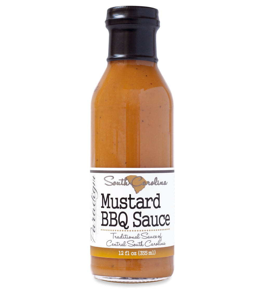 Glass ring neck bottle filled with BBQ sauce on white background. The bottle is labeled, “Paradigm South Carolina Mustard BBQ Sauce – Traditional Sauce of Central South Carolina – 12 fl oz (355ml)”