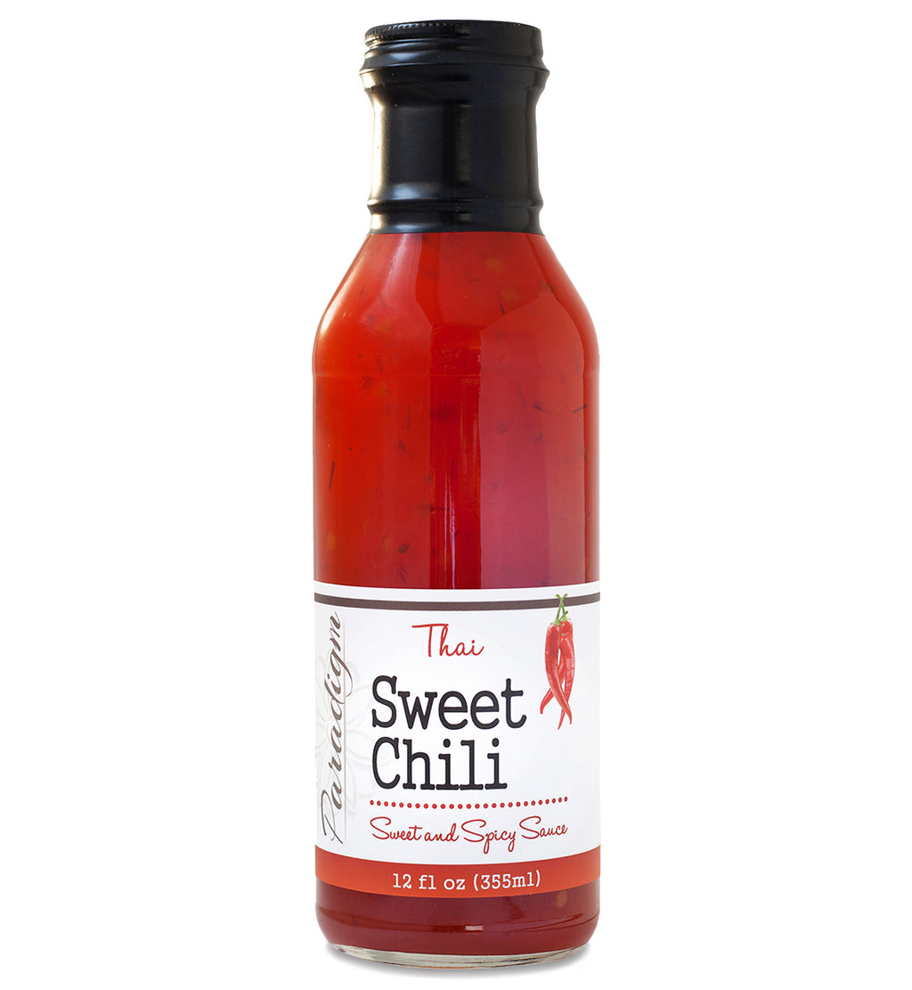 Glass ring neck bottle filled with Thai sweet chili sauce on white background. The bottle is labeled, “Paradigm Thai Sweet Chili Sweet and Spicy Sauce – 12 fl oz (355ml)”