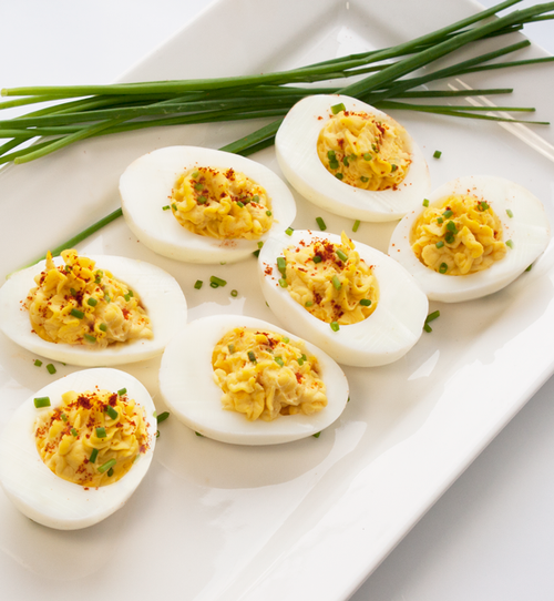Deviled eggs seasoned with chili powder and chives next to a small pile of chives on a rectangular white plate.