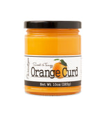 Short, lidded jar full of Orange Curd, on white background. The jar is labeled “Paradigm Sweet & Tangy Orange Curd– Net Weight 10oz (283g)” 