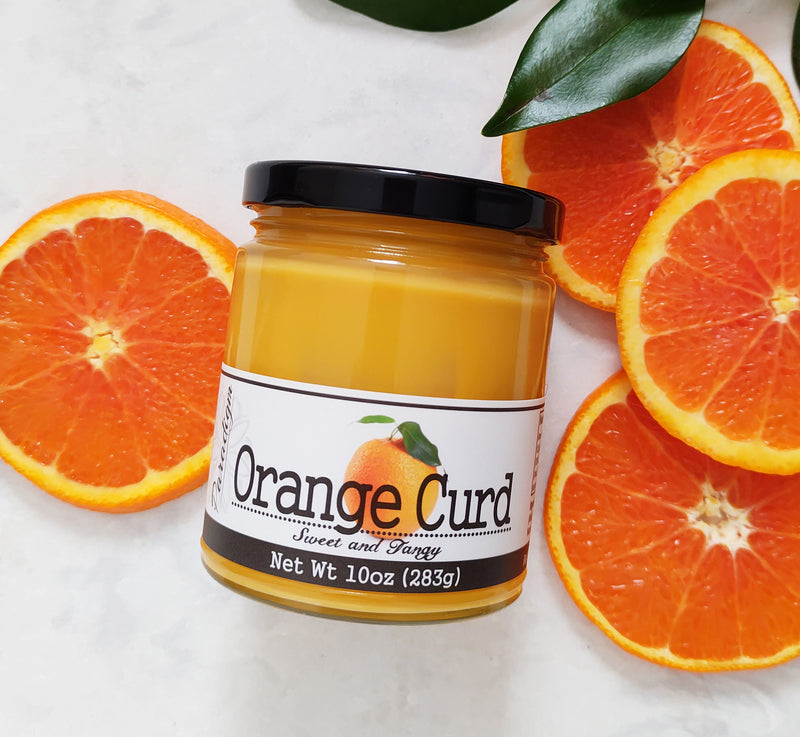 Jar of Orange Curd laying on marble countertop surrounded by round slices of orange and a couple of dark leaves