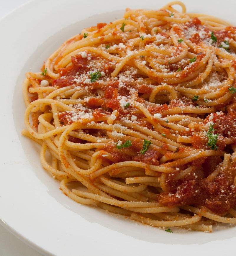Closeup of spaghetti covered in Marinara Sauce, bits of green herbs, and powdered parmesan cheese, all on a white ceramic plate